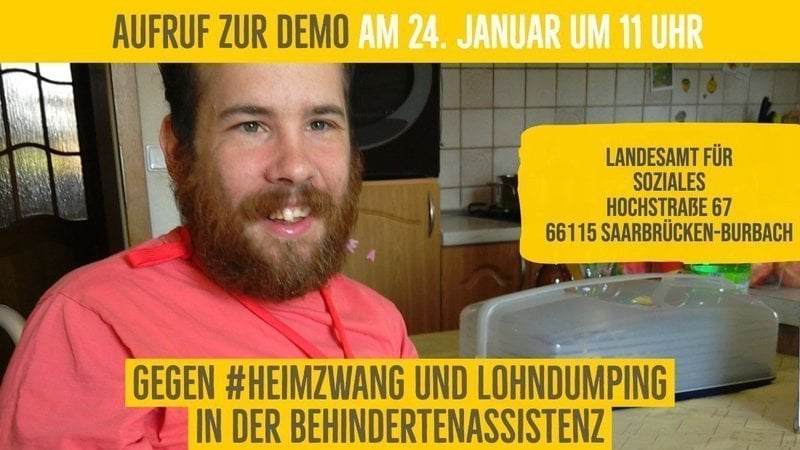 Bild zeigt einen lächelnden bärtigen Mann mit Grafiken zum Termin der Demo gegen Heimzwang. 24. Januar um 11 Uhr. Landesamt für Soziales Hochstraße 67 in 66115 Saarbrücken-Burbach